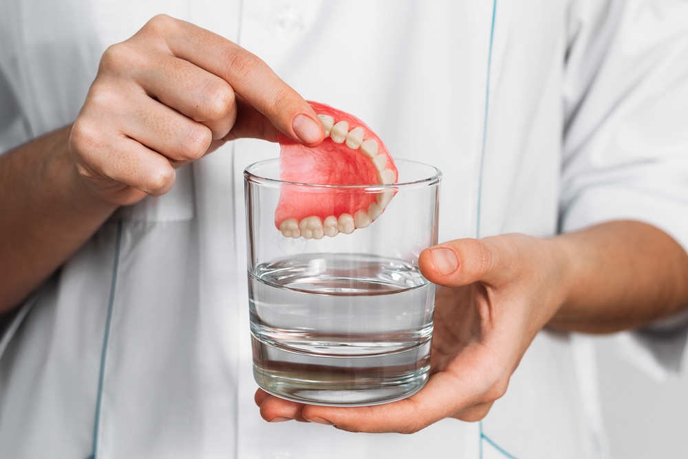 a hand dipping dentures in a cleaning solution in a glass